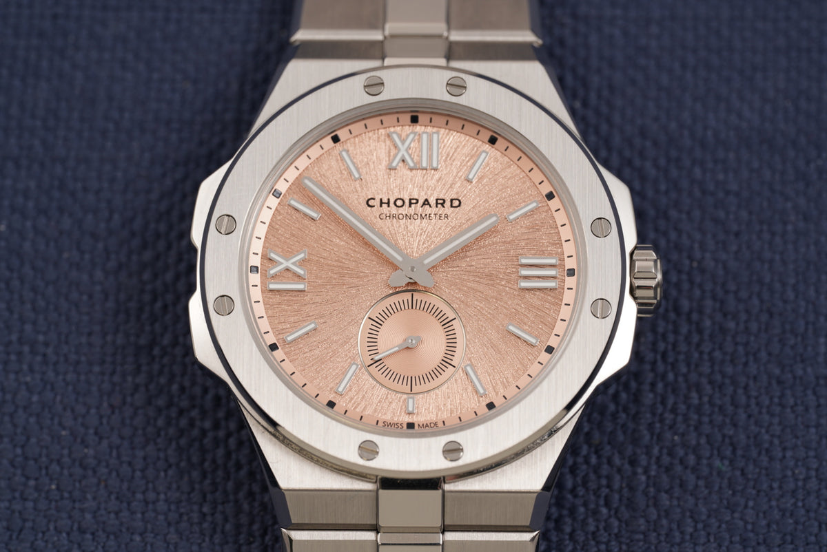 Chopard watch with a brushed silver-tone stainless steel case and bracelet, featuring a textured rose gold dial with Roman numeral hour markers and a small subdial.