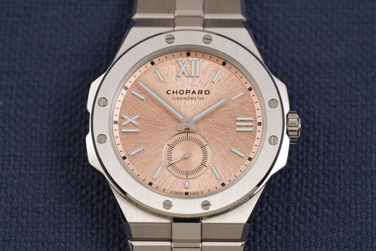 Chopard watch with a brushed silver-tone stainless steel case and bracelet, featuring a textured rose gold dial with Roman numeral hour markers and a small subdial.